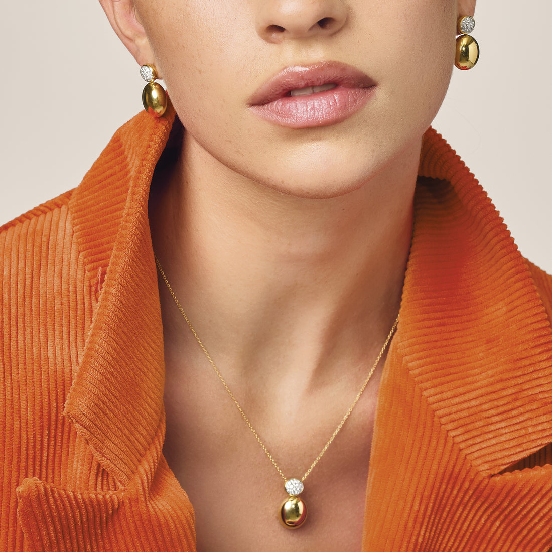 Chimento gold and diamond earrings and pendant worn with a warm orange jacket